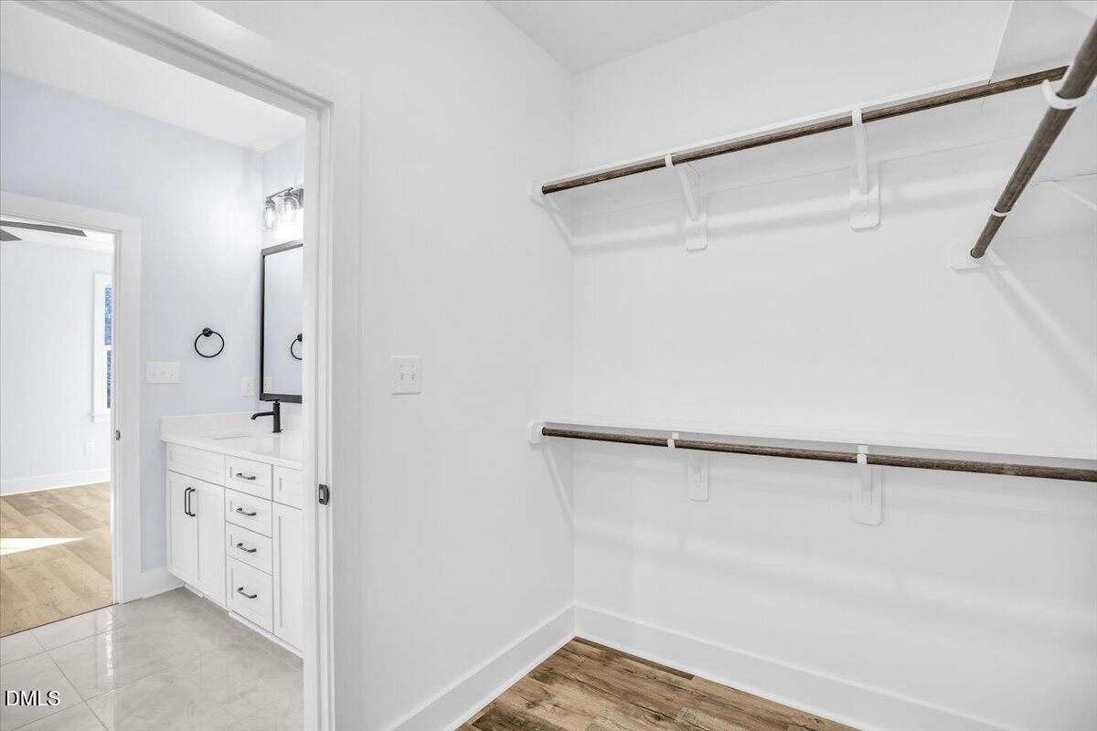 Walk-in closet with two hanging rods and wood-look flooring beside a bathroom vanity.
