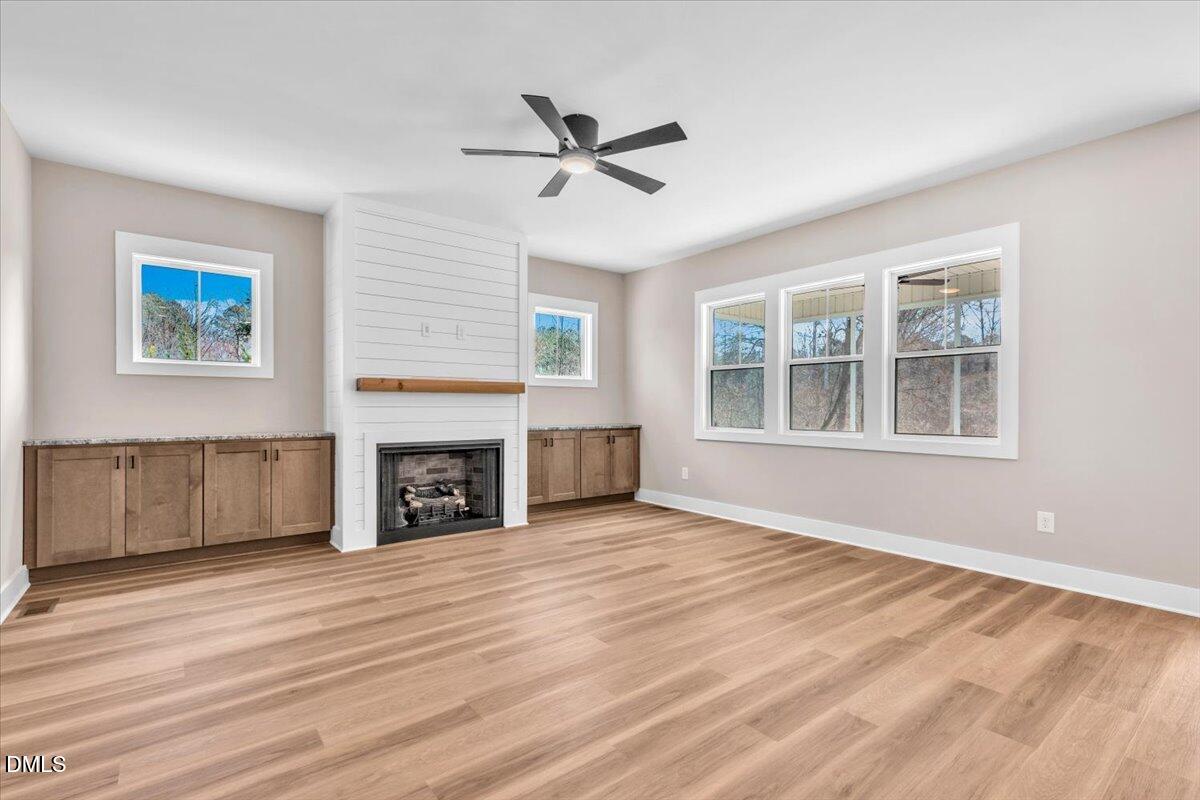 Unfurnished living room with a shiplap fireplace, built-in cabinets, and light wood-look flooring.