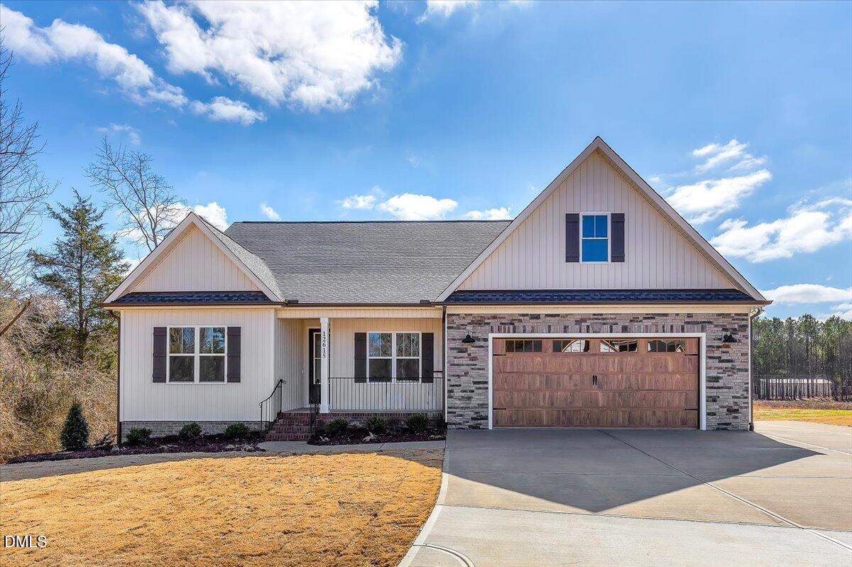 White home with stone accents, covered porch, and two-car garage beneath a partly cloudy sky.