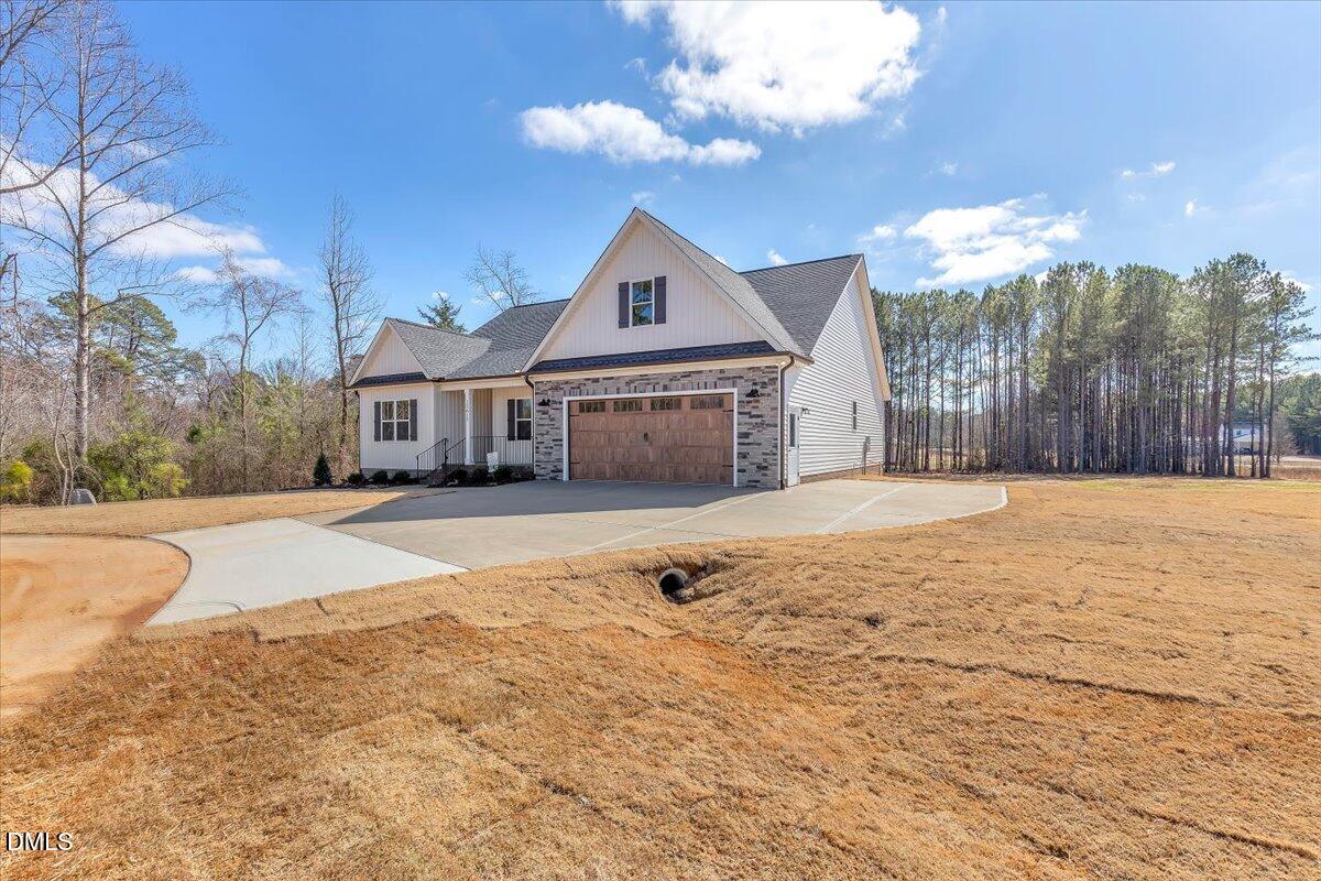 Light-colored home with stone accents, wooden garage door, and a wide driveway.