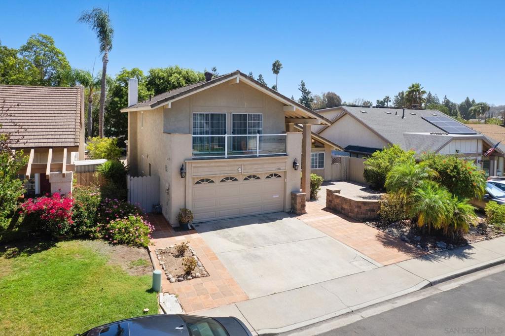 Two-story beige house with a balcony above the garage and a landscaped front yard.