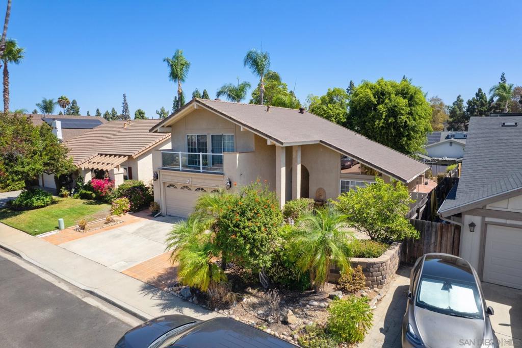 Two-story beige home with a balcony, garage, and landscaped front yard viewed from above.
