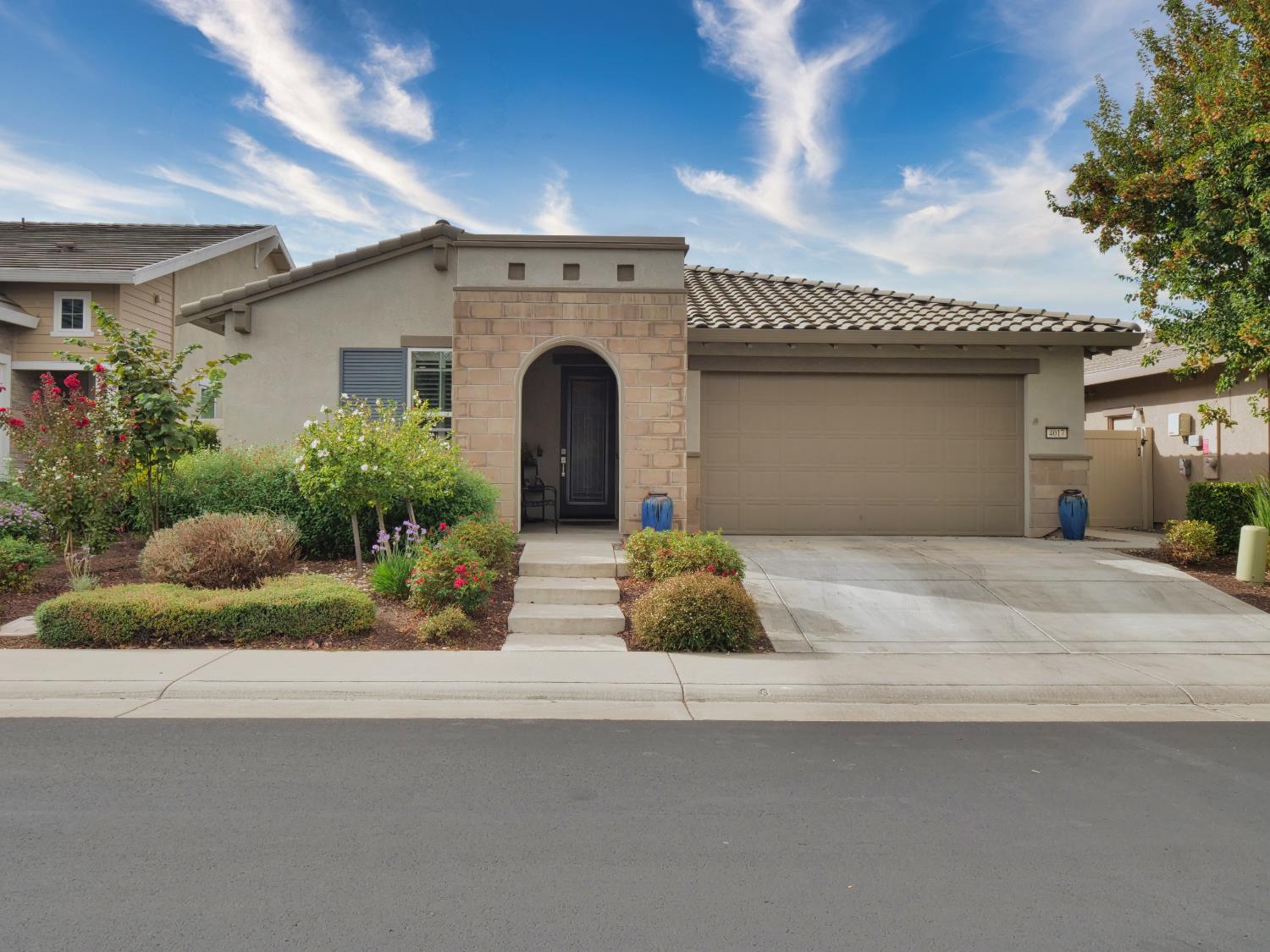 Single-story stucco home with a stone arched entry, two-car garage, and landscaped front yard.