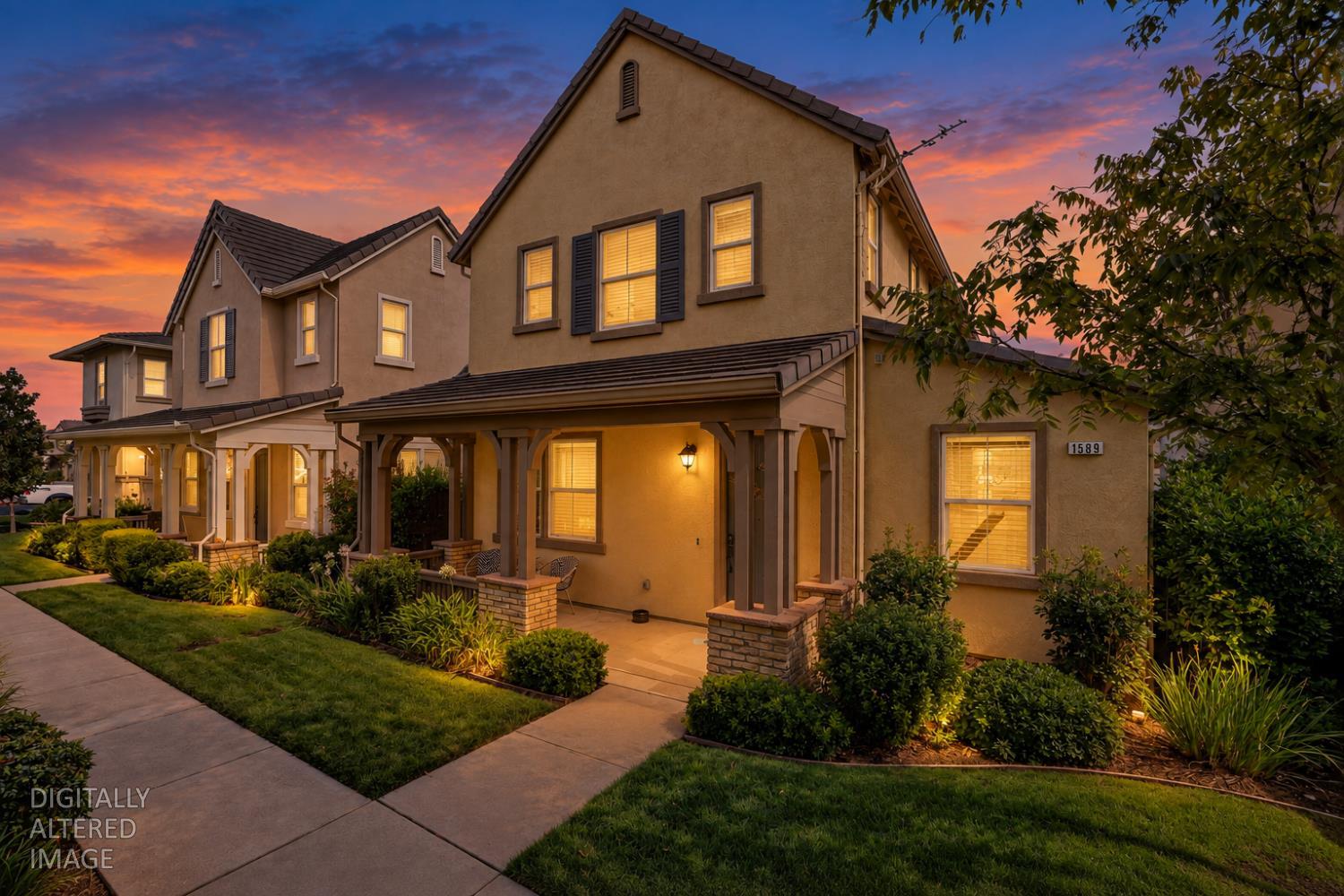 Attached two-story homes with covered porches and glowing windows beneath a colorful dusk sky.