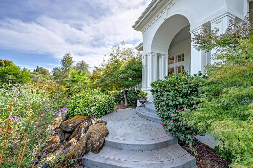 White arched home entrance with curved steps, classical columns, and lush landscaping.