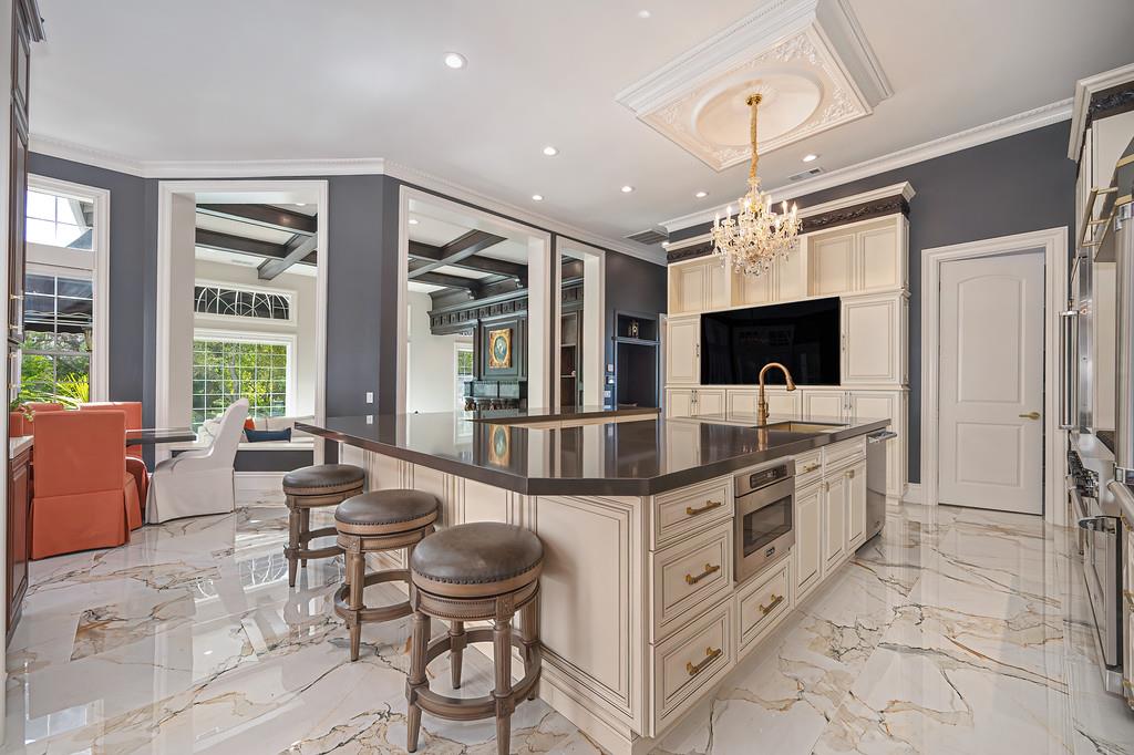 Spacious kitchen with a dark-stone island, white cabinetry, marble floors, and a chandelier.