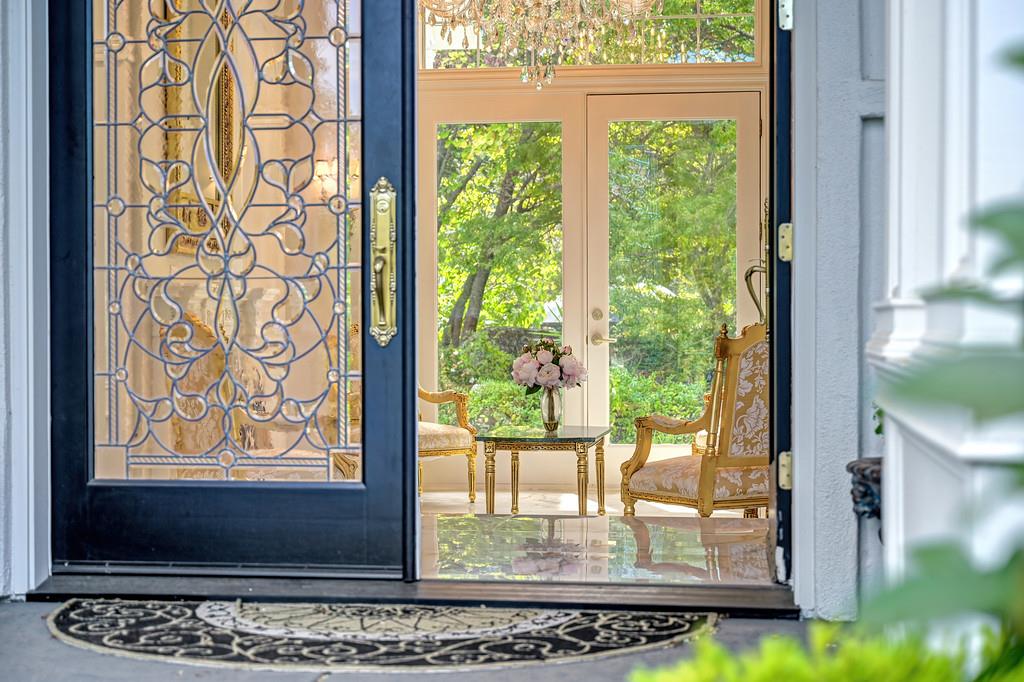 Entry sitting area with an ornate glass front door, upholstered chairs, and leafy garden views.