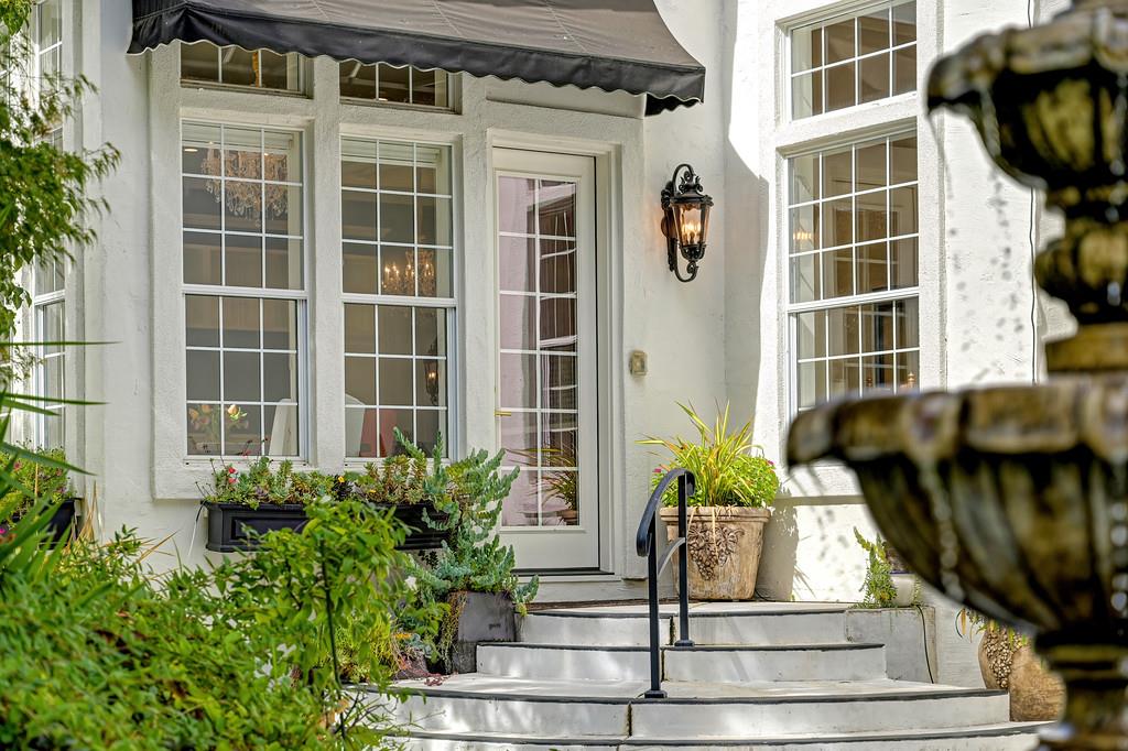 White home entrance with a dark awning, curved steps, potted plants, and a fountain in the foreground.