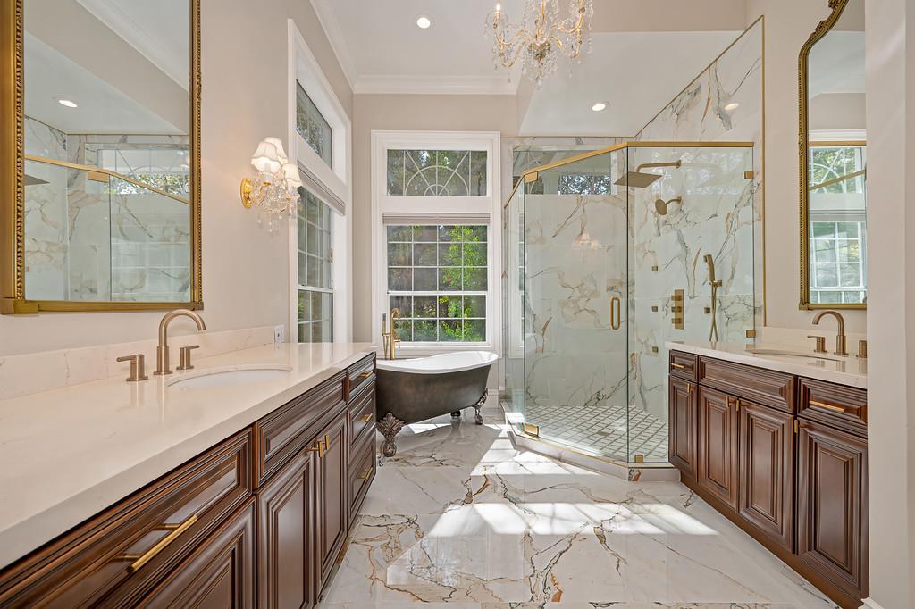 Primary bathroom with a freestanding tub, glass shower, marble surfaces, and dark wood double vanities.