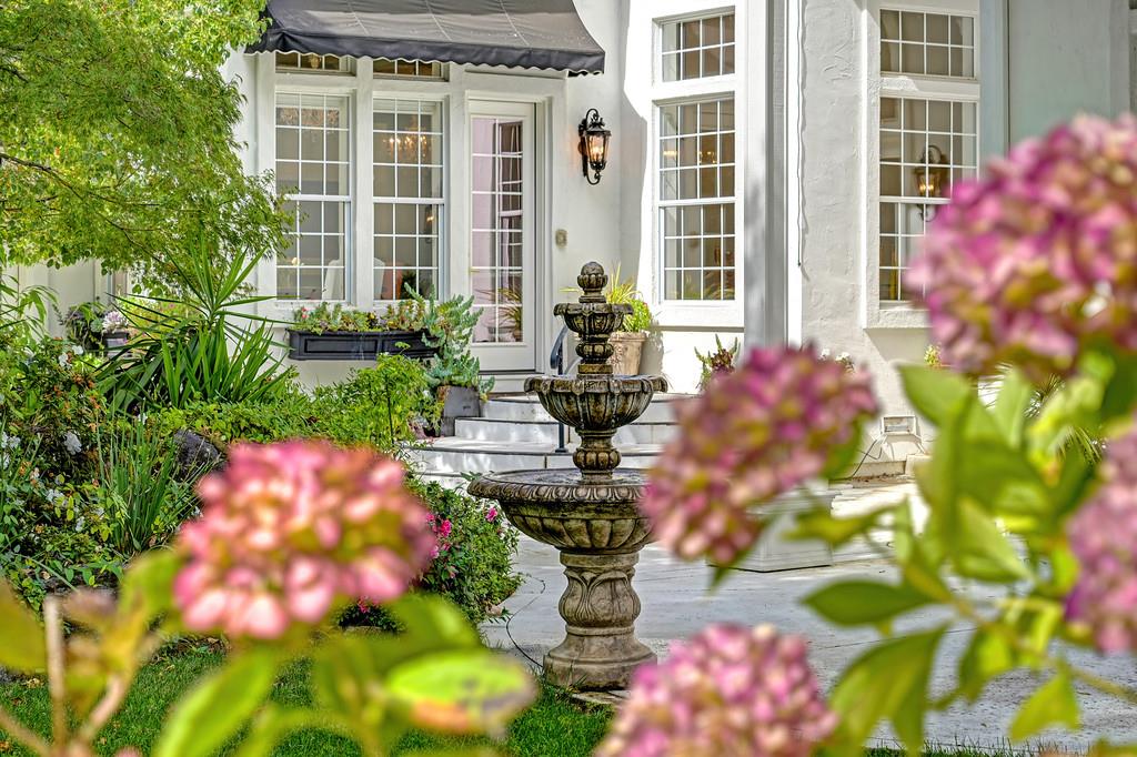Home entrance with a tiered stone fountain and flowering garden beds.
