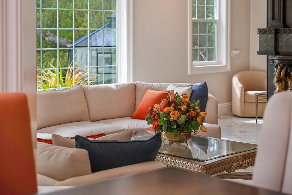 Living room with cream sofas, colorful pillows, a flower arrangement, and large grid-pane windows.