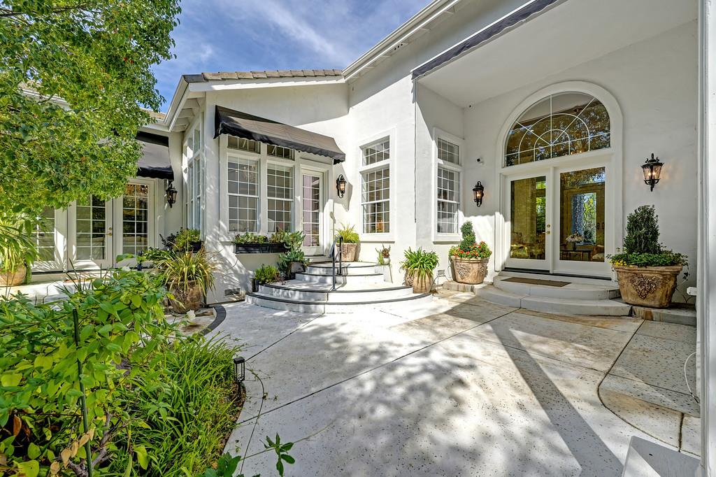 White home entrance with arched window, curved steps, and landscaped stone courtyard.