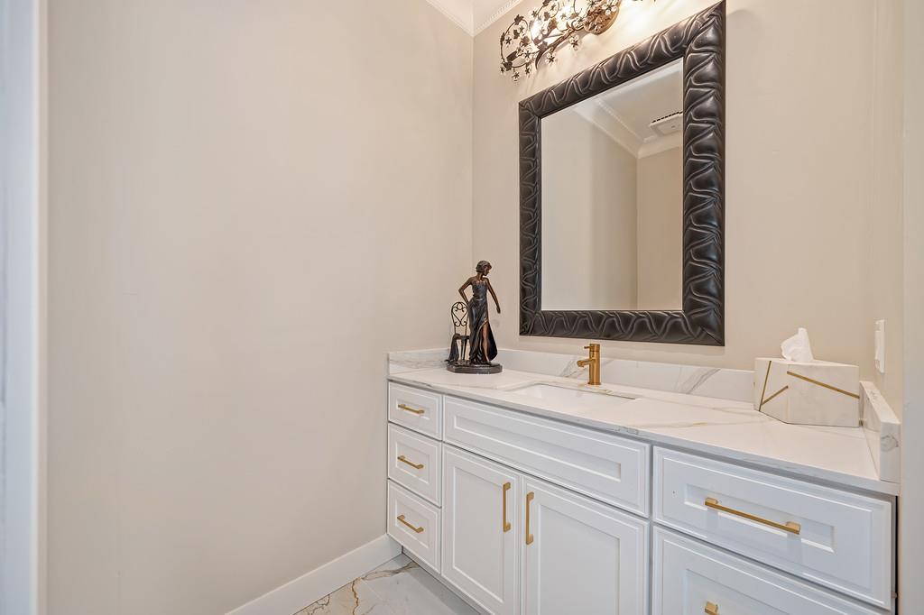 Bathroom vanity with white cabinetry, marble surfaces, gold hardware, and a large dark-framed mirror.