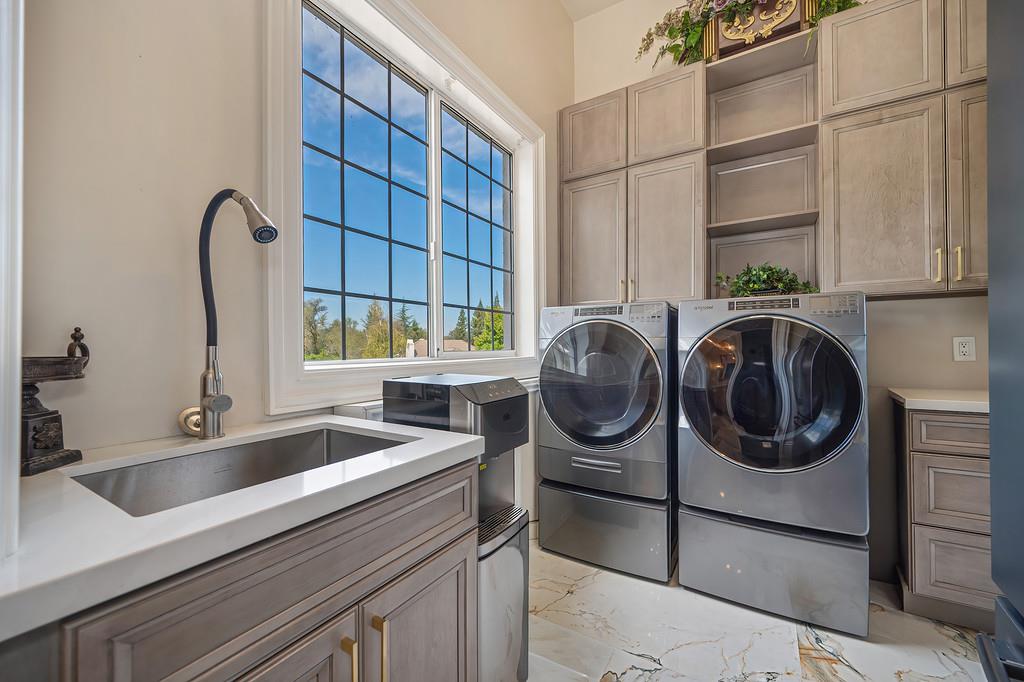 Laundry room with front-loading washer and dryer, utility sink, and built-in cabinetry.