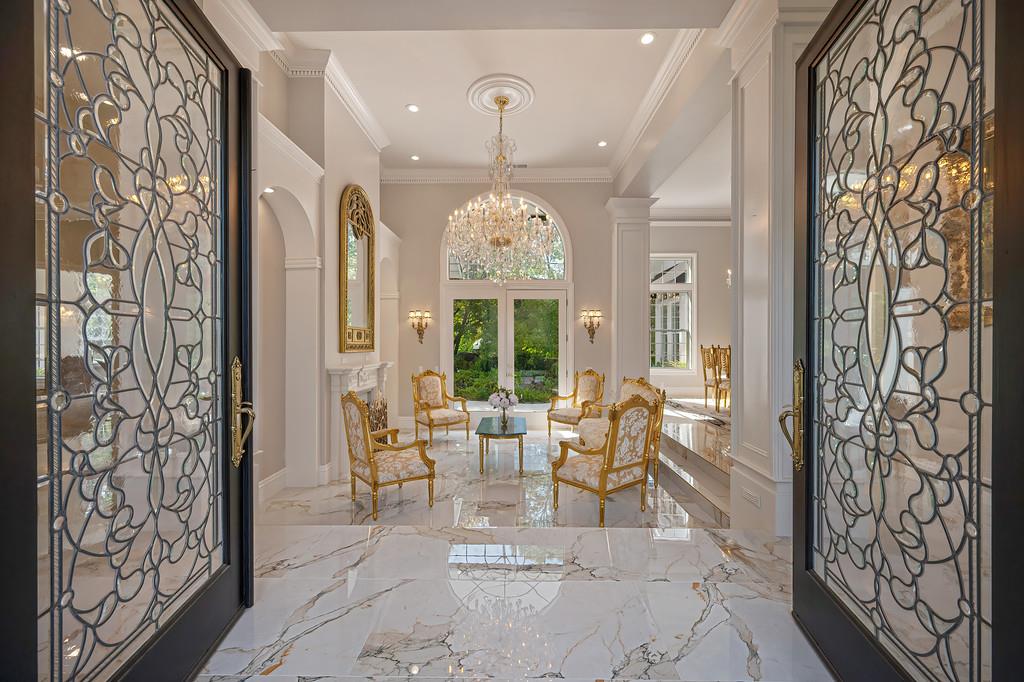 Grand foyer with ornate glass doors, marble flooring, a crystal chandelier, and gold-accented seating.