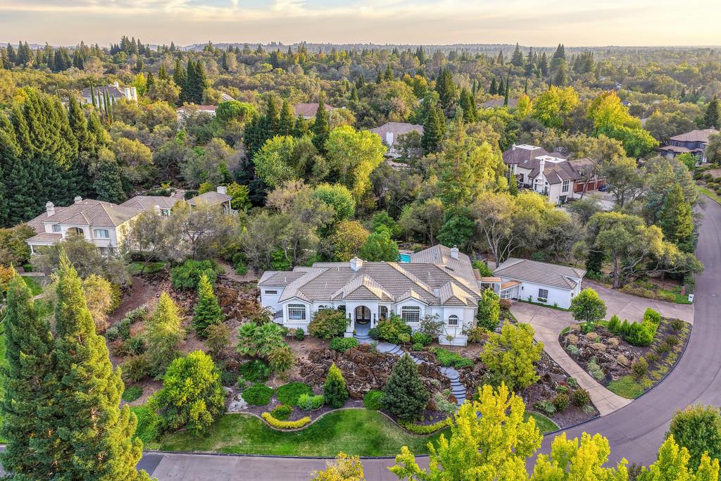 Aerial view of a white home with a landscaped garden and curved driveway, surrounded by mature trees.