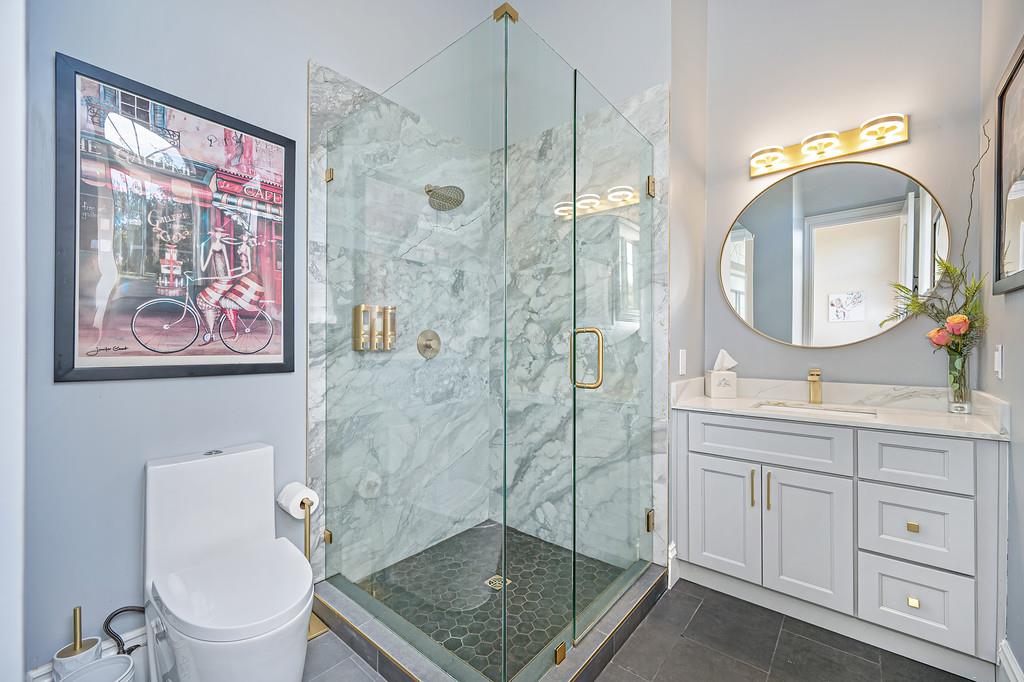 Remodeled bathroom with a marble walk-in shower, glass enclosure, and white vanity.