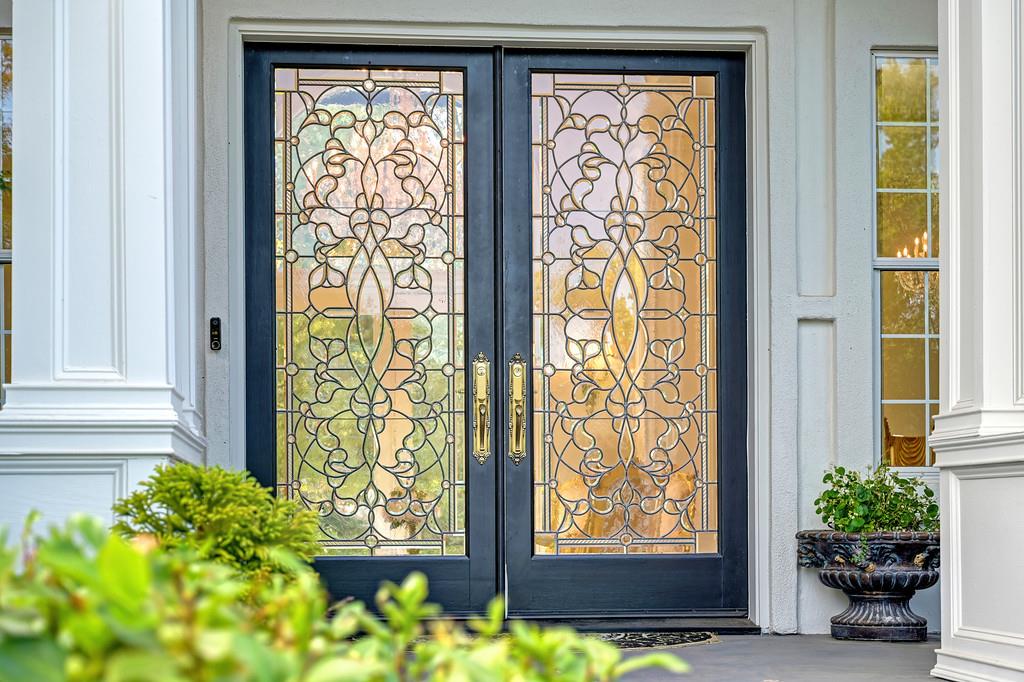 Home entrance with ornate stained-glass double doors, white trim, and a potted plant.