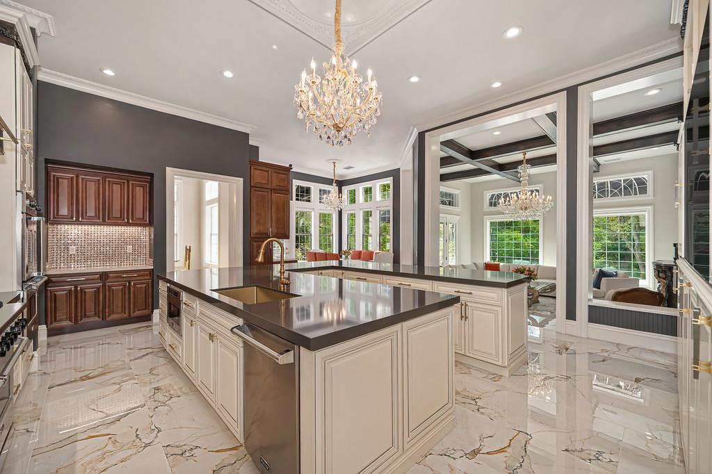 Kitchen with two large islands, dark stone counters, marble flooring, and crystal chandeliers.