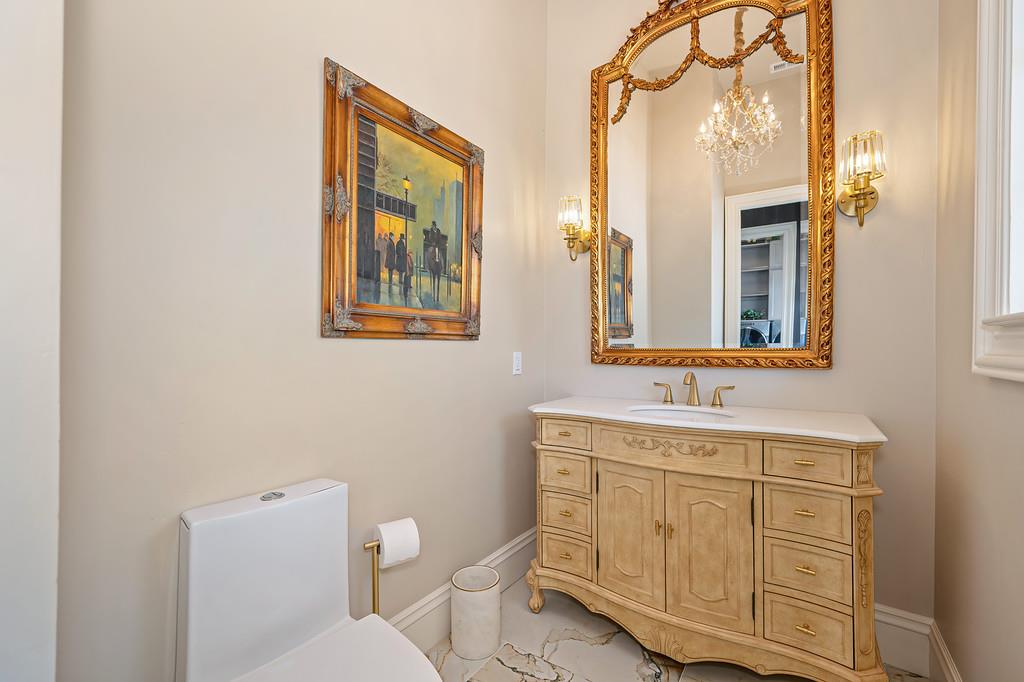 Bathroom with a carved wood vanity, ornate gold-framed mirror, and marble-patterned floor.