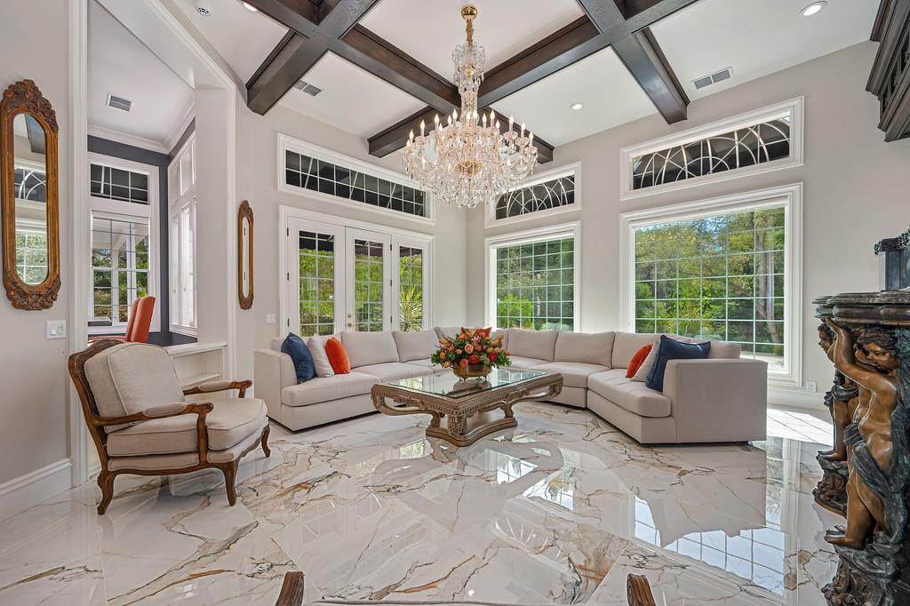 Living room with a cream sectional, crystal chandelier, tall windows, and polished marble floors.