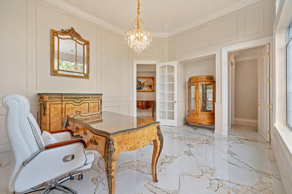 Furnished home office with an ornate glass-topped desk, antique cabinets, and marble flooring.