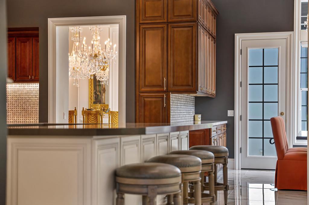 Kitchen with a paneled island, dark wood cabinets, leather stools, and a view of a chandelier-lit dining room.