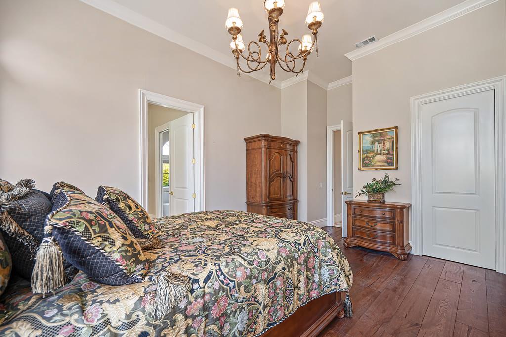 Furnished bedroom with a floral bedspread, brass chandelier, wooden armoire, and hardwood floors.