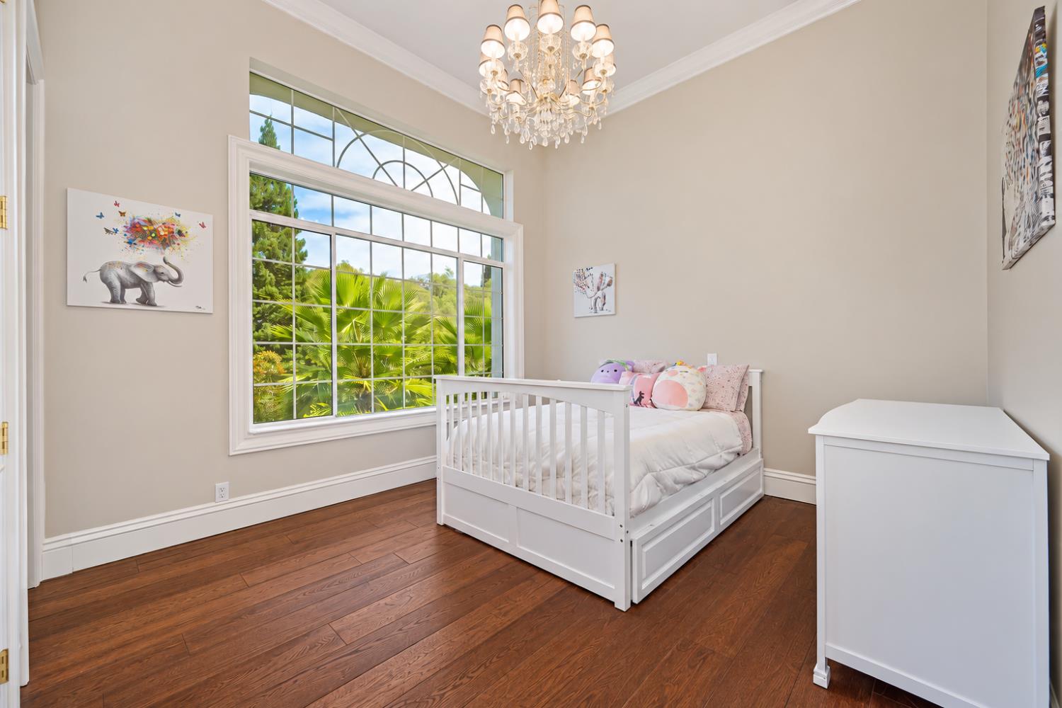 Child's bedroom with a white bed, hardwood floors, and a large window overlooking greenery.
