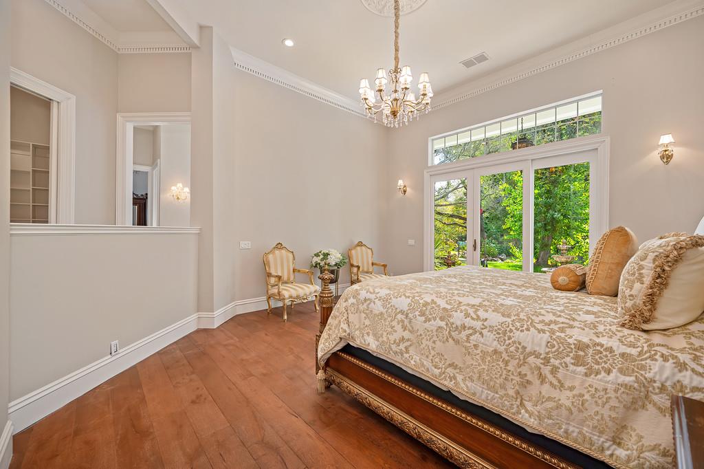 Bedroom with a carved wooden bed, crystal chandelier, and tall garden-facing glass doors.