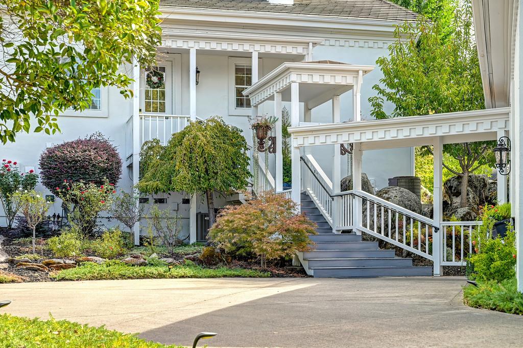 White home with a covered porch and broad steps beside landscaped gardens and a driveway.