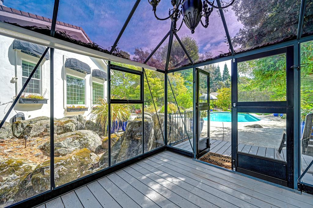 Screened-in porch opening onto a pool deck, with a chandelier overhead and garden rocks along the house.