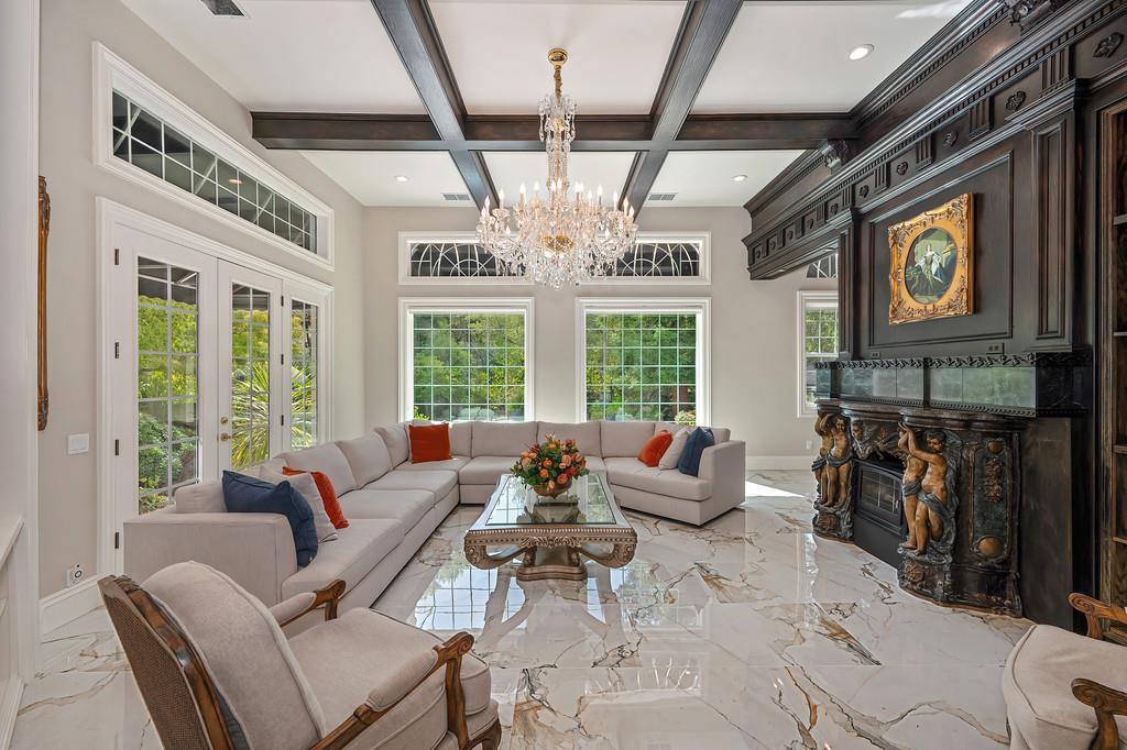 Living room with a crystal chandelier, coffered ceiling, marble floors, and ornate carved fireplace.