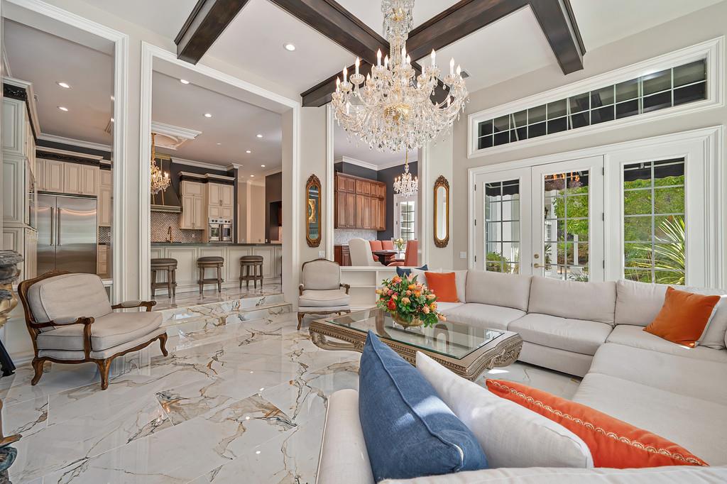 Living room with a white sectional, marble floors, dark ceiling beams, and a crystal chandelier.