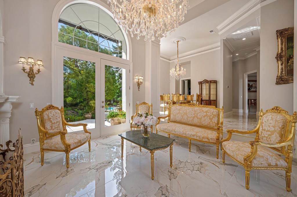 Formal living room with ornate gold seating, marble floors, and tall arched glass doors to the garden.