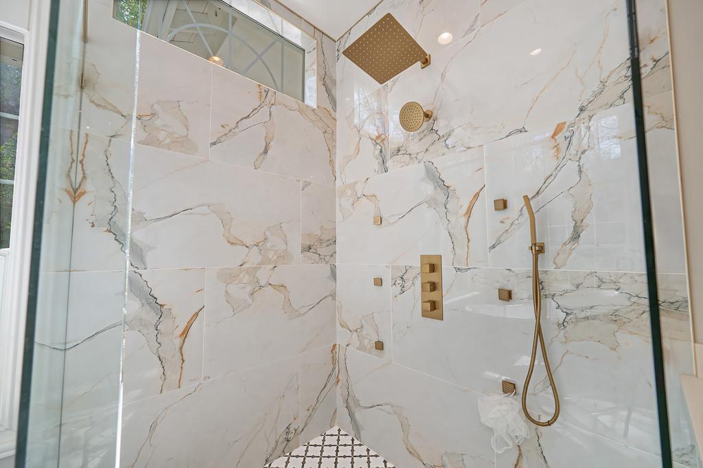 Walk-in shower with dramatic veined tile, gold fixtures, and a glass enclosure.