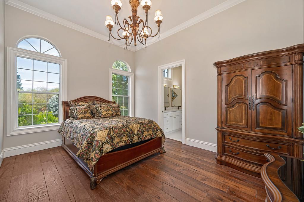 Bedroom with floral bedding, carved wooden furniture, arched windows, and an ornate chandelier.