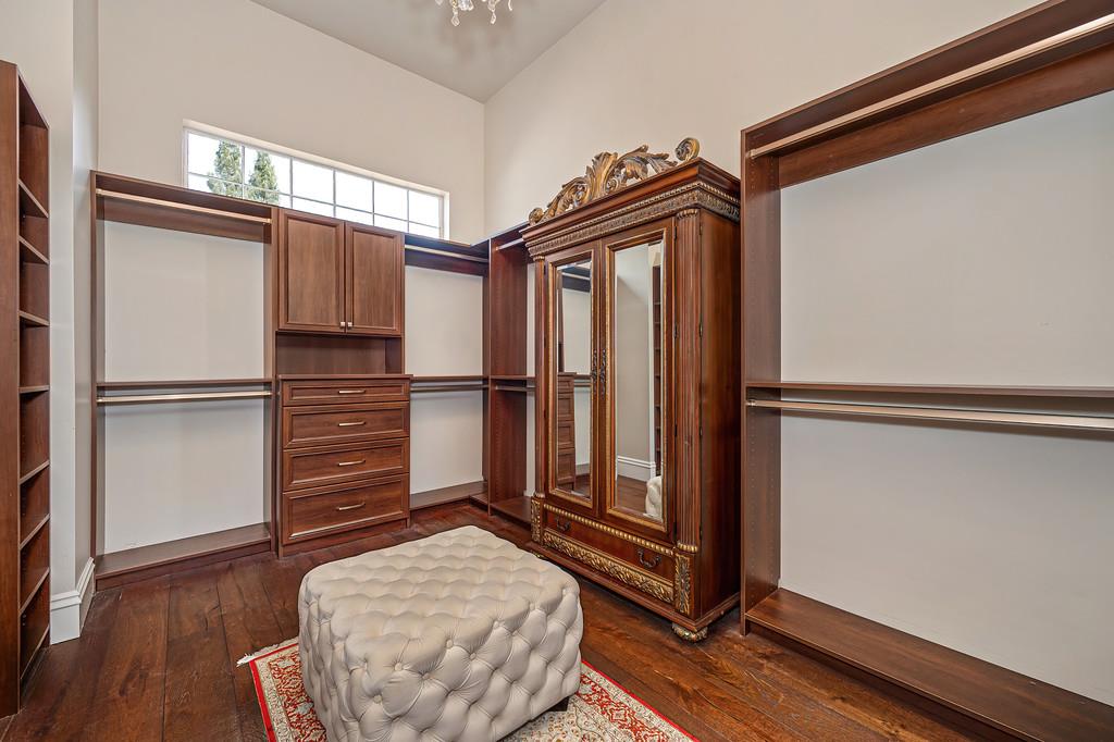 Walk-in closet with dark wood cabinetry, ornate mirrored armoire, and tufted ottoman.