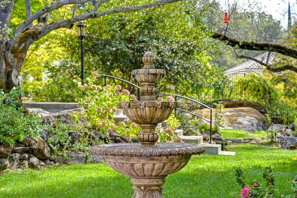 Tiered stone fountain in a garden with flowering shrubs and stone steps.