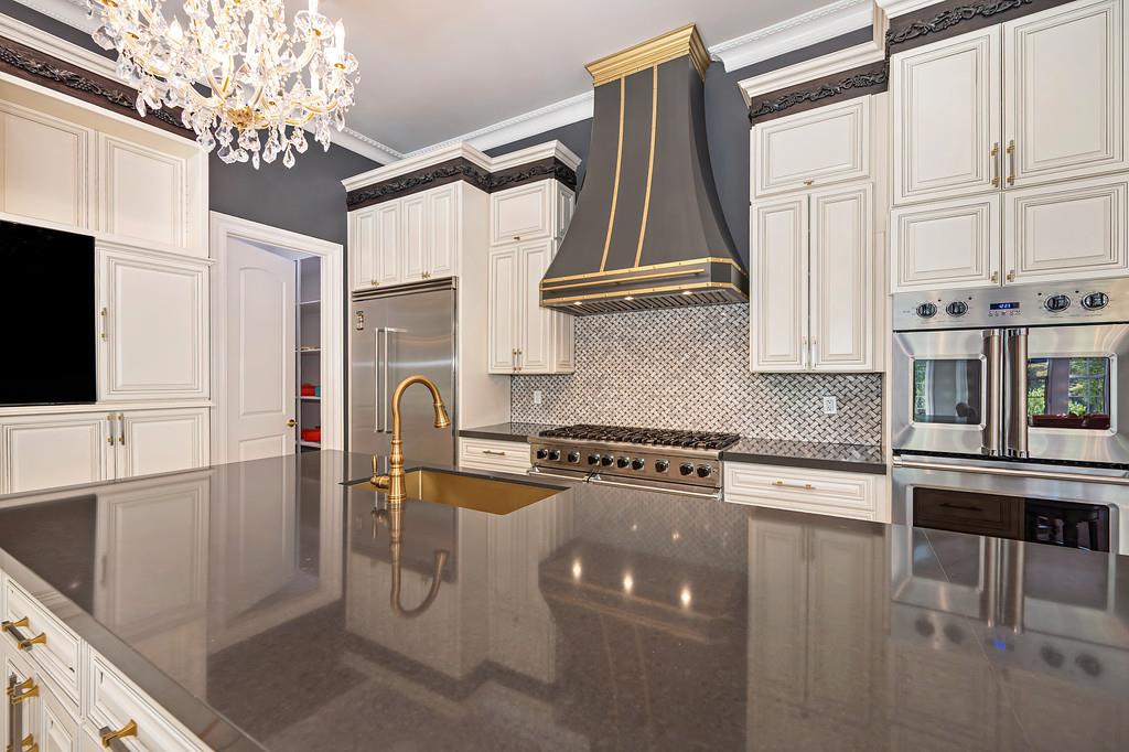Luxury kitchen with white cabinetry, a reflective stone island, brass faucet, and stainless steel appliances.