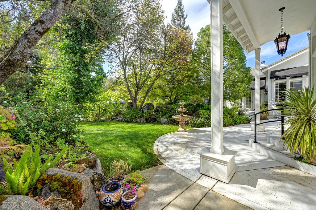 Landscaped backyard garden and curved patio with a fountain, mature trees, and covered seating.