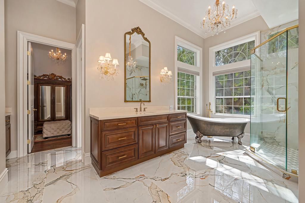 Bathroom with a dark wood vanity, freestanding tub beneath tall windows, and glass-enclosed shower.
