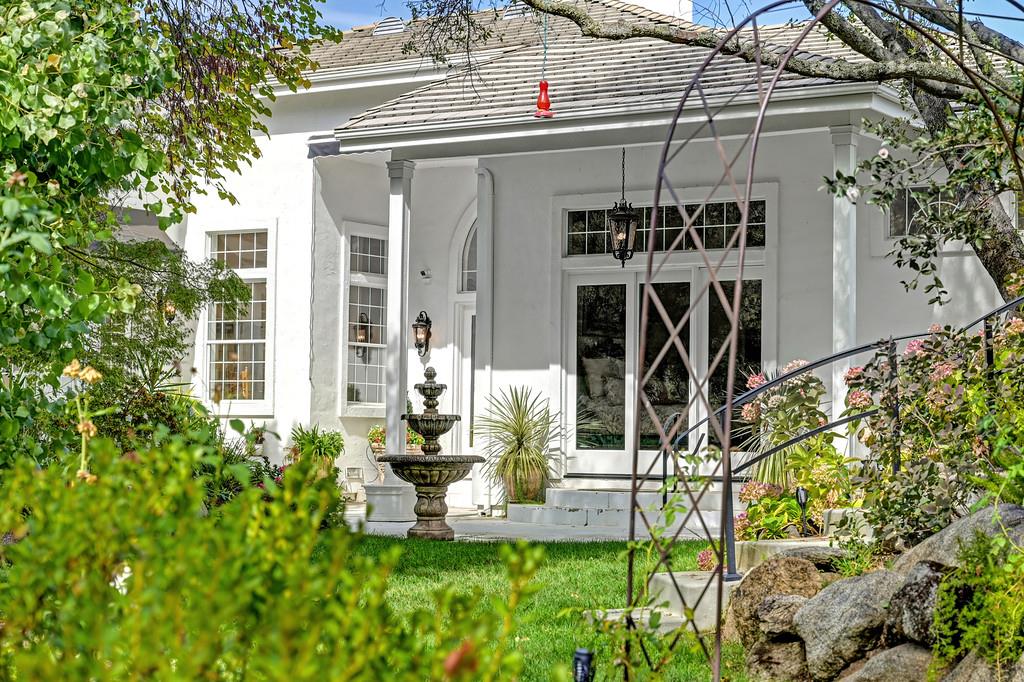 White house exterior with tall glass doors, a tiered fountain, and a leafy garden.