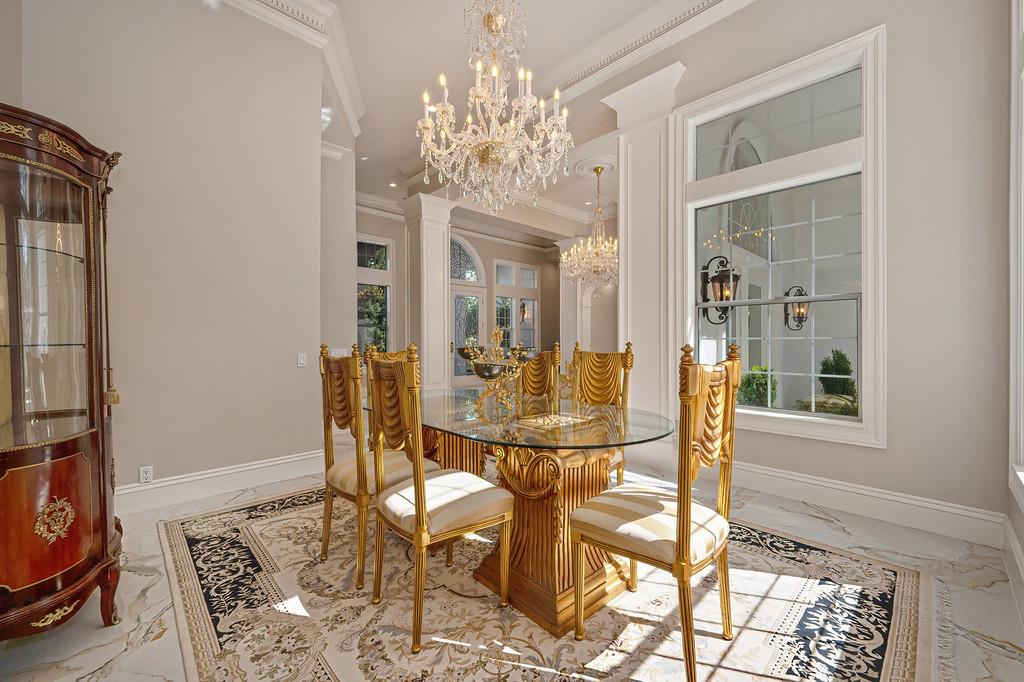 Formal dining room with ornate gold furniture, crystal chandeliers, and large sunlit windows.