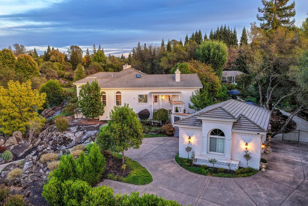Large home with tiled roofs and curved driveway, surrounded by landscaped grounds and autumn trees.