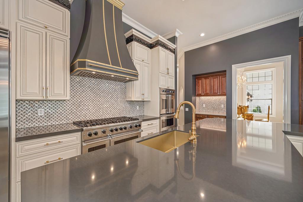 Kitchen with a large gray island, brass sink, commercial range, and patterned tile backsplash.