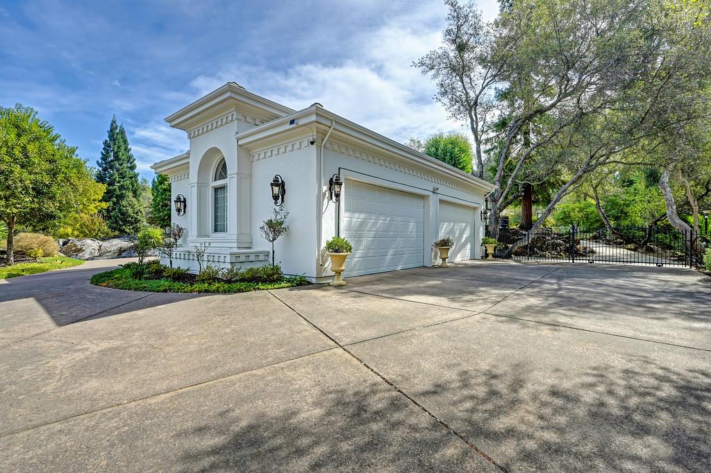 White garage with multiple doors beside a broad concrete driveway and mature trees.