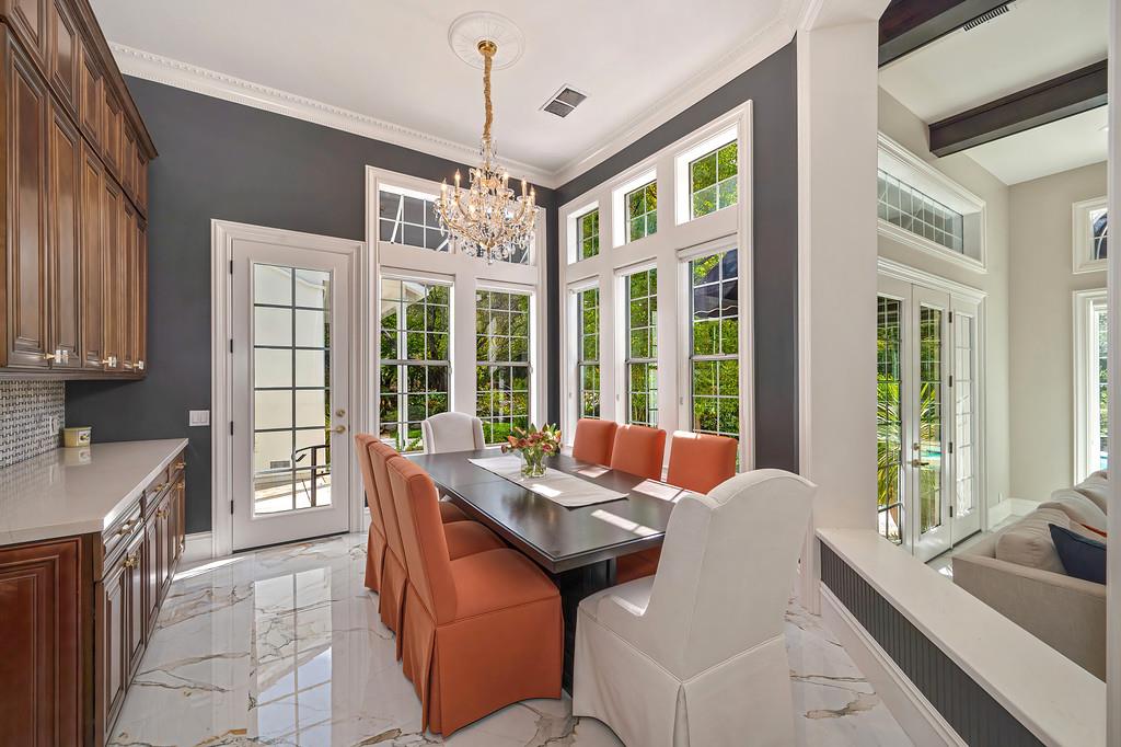 Dining room with a crystal chandelier, tall windows, dark table, and orange and white chairs.