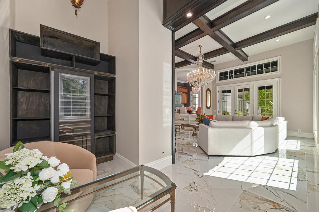Bright living room with marble floors, dark built-in shelves, ceiling beams, and a chandelier.