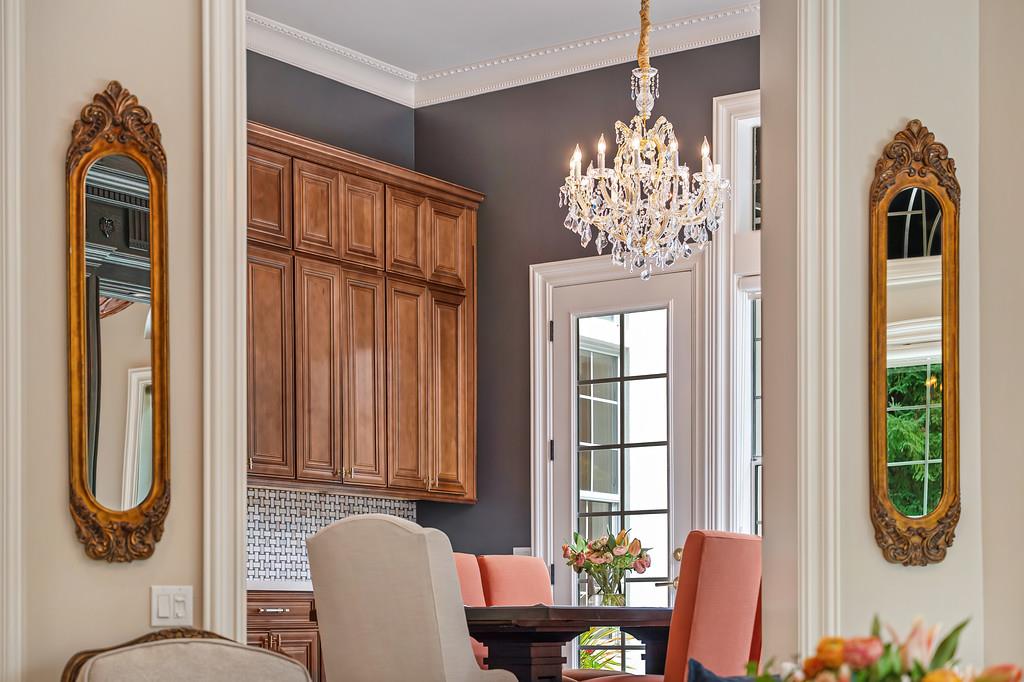 Dining room with a crystal chandelier, coral chairs, tall wood cabinets and glass-paneled doors.